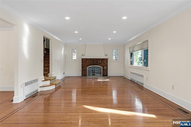 unfurnished living room featuring a brick fireplace, radiator, baseboards, and wood finished floors