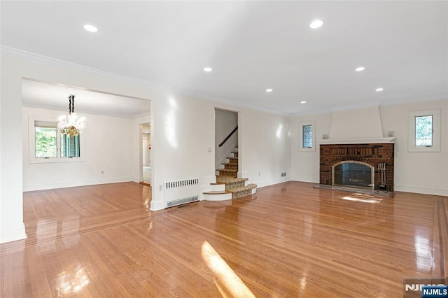 unfurnished living room featuring radiator heating unit, light wood-style flooring, ornamental molding, stairs, and a fireplace