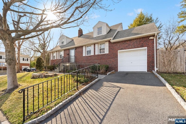 cape cod house with fence, driveway, an attached garage, a chimney, and brick siding