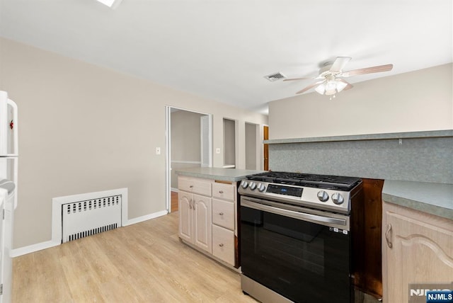 kitchen featuring visible vents, light wood-type flooring, radiator heating unit, stainless steel gas stove, and a ceiling fan