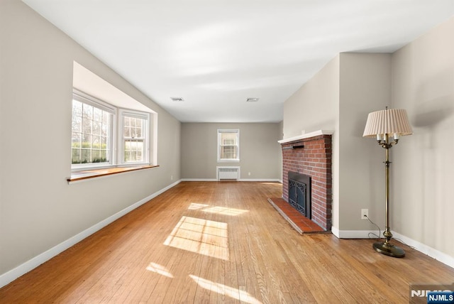 unfurnished living room with visible vents, hardwood / wood-style floors, radiator, a fireplace, and baseboards