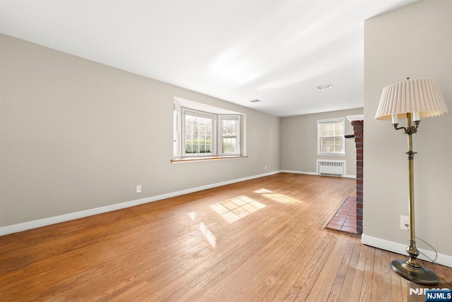 unfurnished room with light wood finished floors, visible vents, radiator, and baseboards