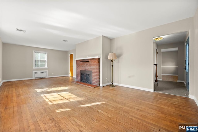 unfurnished living room with visible vents, a brick fireplace, baseboards, radiator heating unit, and hardwood / wood-style floors