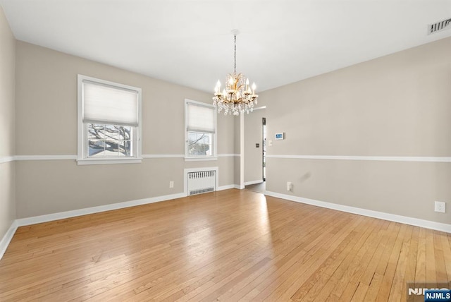 unfurnished room with hardwood / wood-style flooring, radiator heating unit, baseboards, and a chandelier