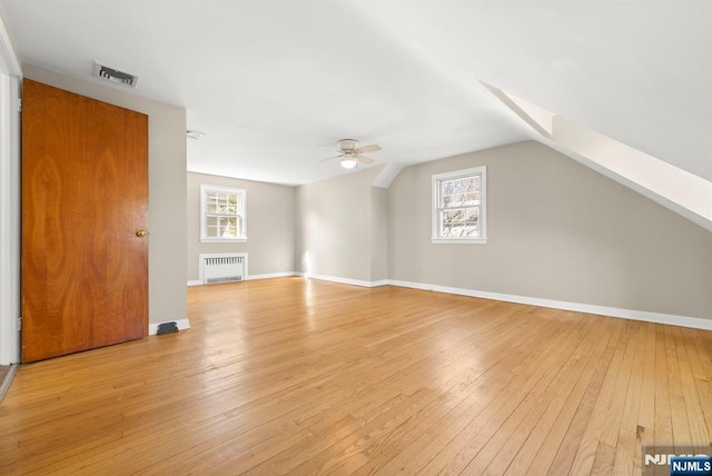 additional living space with visible vents, a ceiling fan, light wood-style floors, radiator, and vaulted ceiling