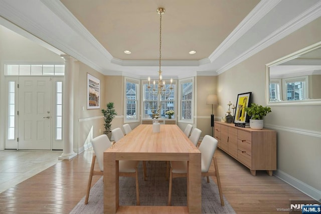 dining room featuring ornate columns, light wood-style flooring, a tray ceiling, and ornamental molding