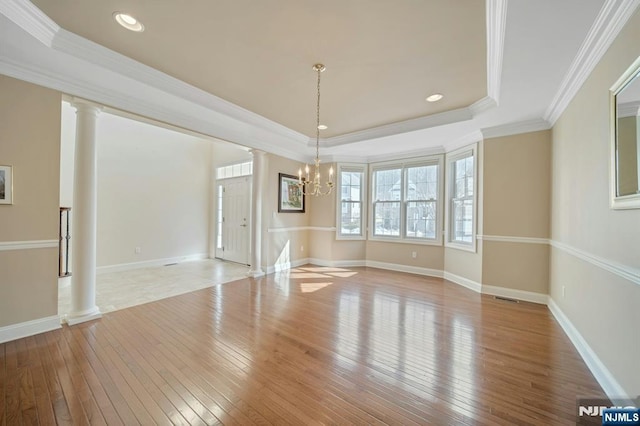 unfurnished dining area featuring ornate columns, light wood-style flooring, a tray ceiling, and ornamental molding