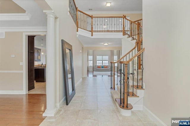 foyer entrance with ornamental molding, a high ceiling, decorative columns, and baseboards