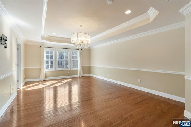 unfurnished room with an inviting chandelier, wood-type flooring, a tray ceiling, and baseboards