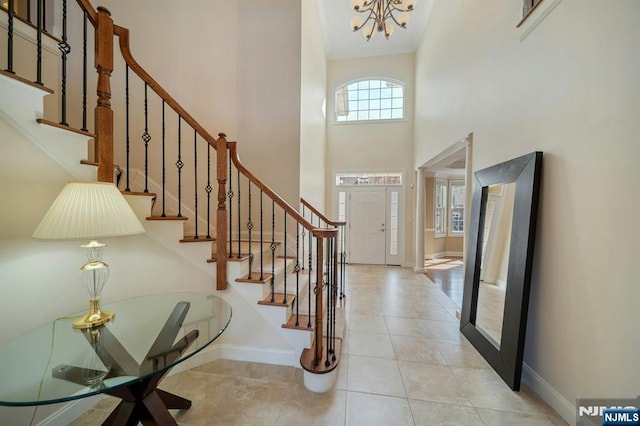 foyer entrance featuring light tile patterned floors, a high ceiling, a chandelier, baseboards, and stairs