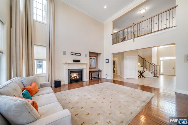 living area featuring light wood-style flooring, ornamental molding, a glass covered fireplace, baseboards, and stairs