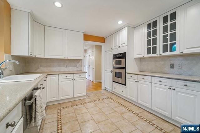 kitchen with stainless steel double oven, a sink, white cabinets, and recessed lighting