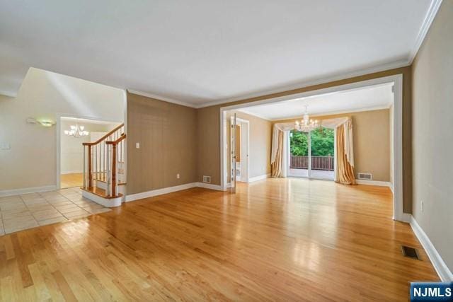 unfurnished living room featuring visible vents, stairway, ornamental molding, wood finished floors, and an inviting chandelier