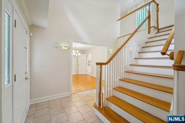 tiled entrance foyer featuring baseboards, a high ceiling, stairway, and a notable chandelier