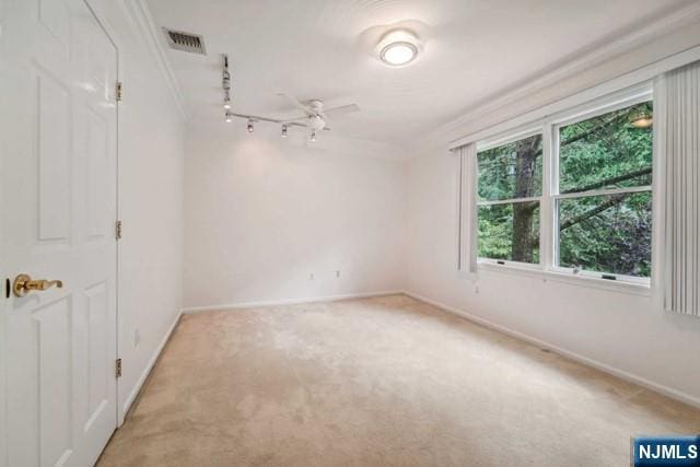 unfurnished room with crown molding, light colored carpet, visible vents, track lighting, and baseboards