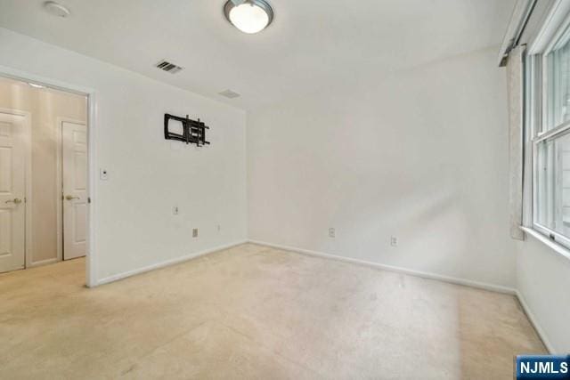 unfurnished room with baseboards, visible vents, and light colored carpet