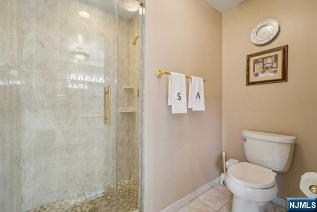 bathroom with a stall shower, baseboards, toilet, and tile patterned floors