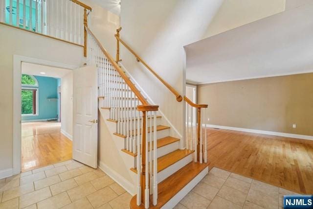 stairway featuring a towering ceiling, baseboards, and wood finished floors