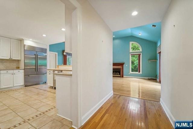 hallway with vaulted ceiling, light wood-type flooring, visible vents, and baseboards