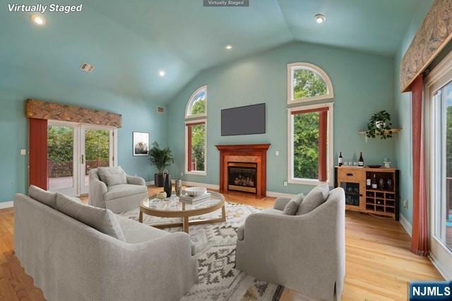 living room featuring visible vents, baseboards, light wood-style flooring, a fireplace, and high vaulted ceiling