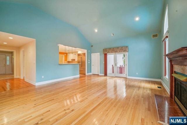 unfurnished living room featuring visible vents, baseboards, a fireplace with flush hearth, wood finished floors, and high vaulted ceiling