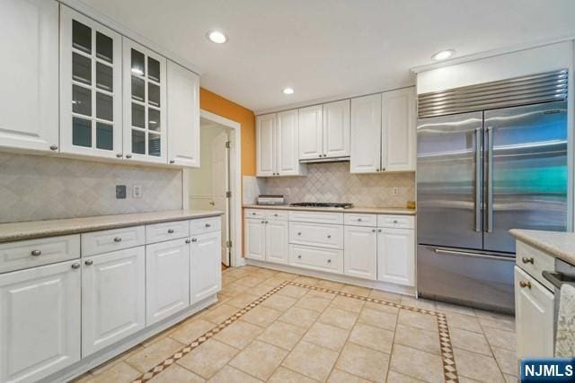 kitchen with built in fridge, recessed lighting, white cabinets, light countertops, and glass insert cabinets