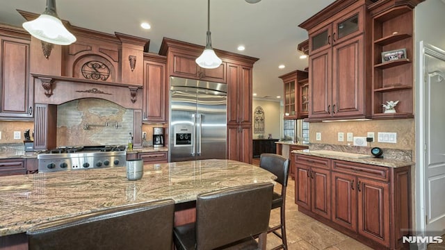 kitchen featuring a breakfast bar area, decorative light fixtures, appliances with stainless steel finishes, open shelves, and glass insert cabinets