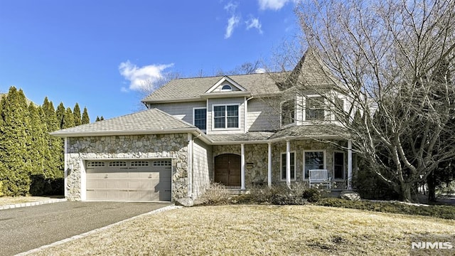 victorian home featuring a garage, stone siding, covered porch, and driveway