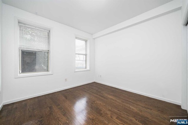 unfurnished room with dark wood-style flooring and baseboards