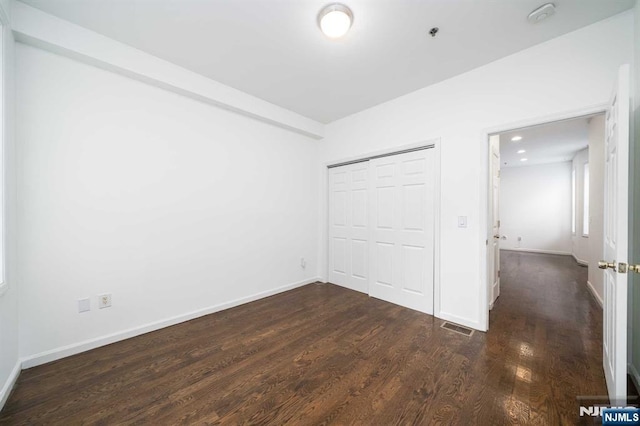 unfurnished bedroom with baseboards, visible vents, dark wood finished floors, and a closet