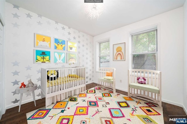 bedroom featuring wood finished floors, a chandelier, a nursery area, baseboards, and wallpapered walls