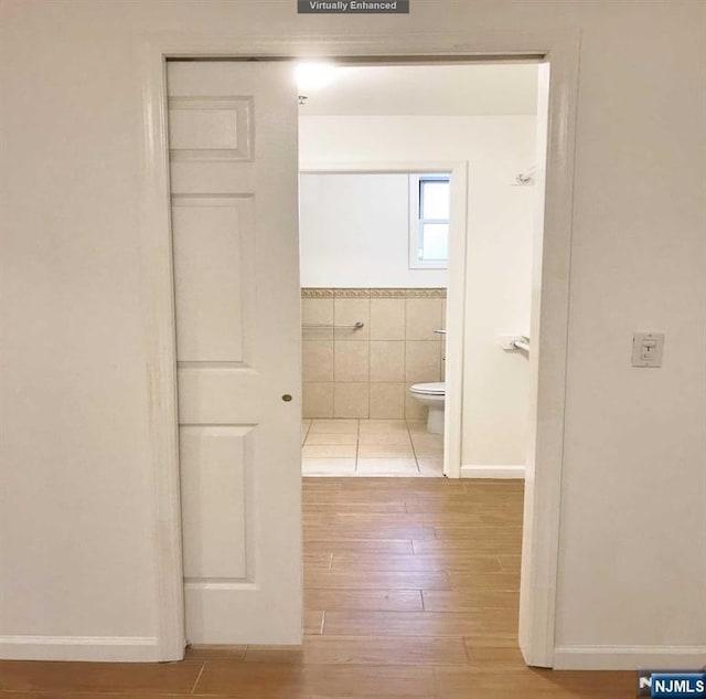 bathroom with toilet, wood finished floors, and tile walls