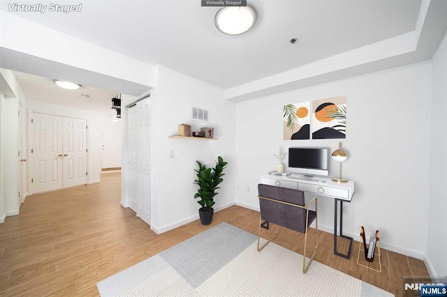 office space with baseboards, a barn door, visible vents, and wood finished floors