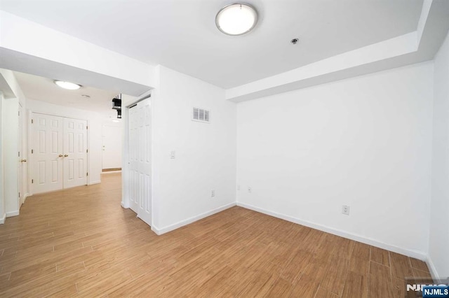 unfurnished room featuring light wood-type flooring, visible vents, baseboards, and a barn door