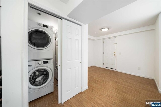 laundry area with laundry area, light wood finished floors, stacked washer / dryer, and baseboards