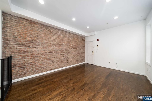 spare room featuring brick wall, recessed lighting, wood finished floors, and baseboards