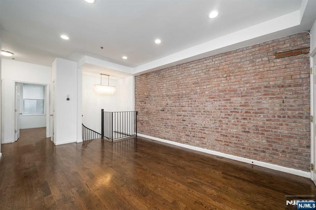 unfurnished room featuring brick wall, wood finished floors, and recessed lighting