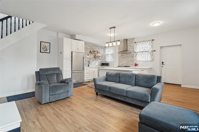 living area featuring light wood-style flooring, stairs, and baseboards