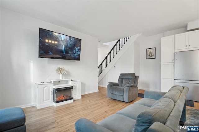 living area featuring light wood-type flooring, a warm lit fireplace, baseboards, and stairway