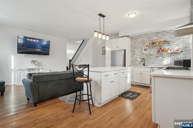 kitchen featuring stainless steel appliances, tasteful backsplash, light countertops, open floor plan, and light wood-type flooring