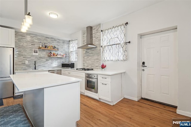 kitchen featuring stainless steel appliances, white cabinetry, light wood-type flooring, backsplash, and wall chimney exhaust hood