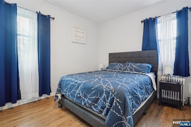 bedroom featuring radiator heating unit, multiple windows, and wood finished floors