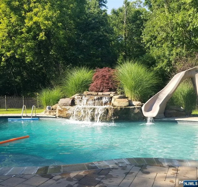 view of swimming pool featuring a water slide and fence