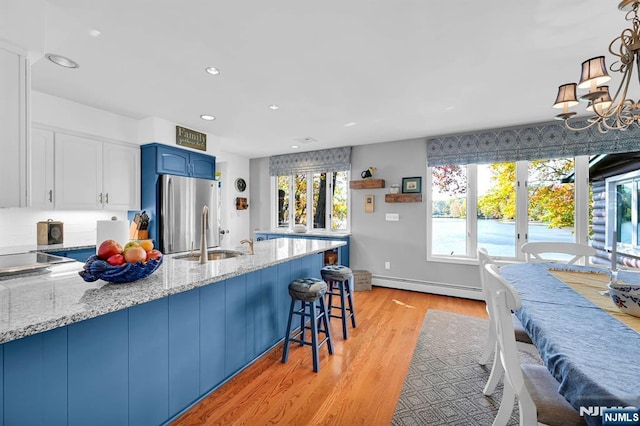 kitchen with a baseboard radiator, a peninsula, a sink, blue cabinetry, and freestanding refrigerator