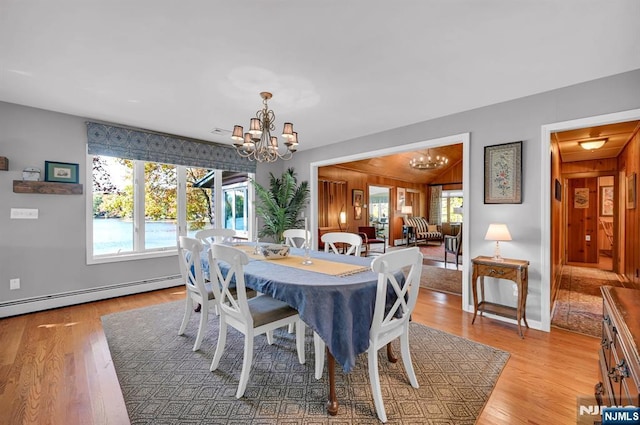 dining room featuring light wood finished floors, a healthy amount of sunlight, baseboard heating, and an inviting chandelier