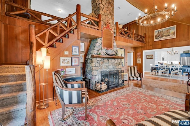 living room with stairway, a high ceiling, a stone fireplace, wooden walls, and wood finished floors