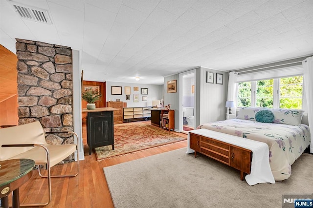 bedroom featuring ensuite bathroom, wood finished floors, and visible vents