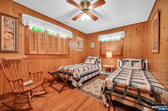 bedroom featuring wood walls, visible vents, a baseboard heating unit, and wood finished floors