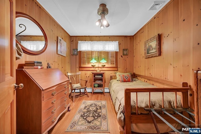 bedroom featuring ornamental molding, light wood-type flooring, visible vents, and wood walls