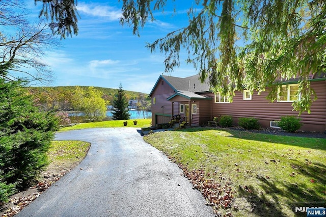 view of front facade with aphalt driveway, log veneer siding, a front yard, and a water view